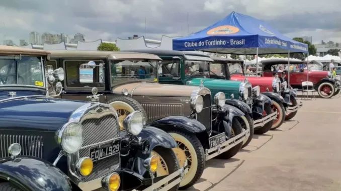 Encontro e Exposição de Veículos Antigos no Campo de Marte, em São Paulo: fila de carros clássicos e caminhões antigos sob tendas e céu nublado, com público ao fundo.