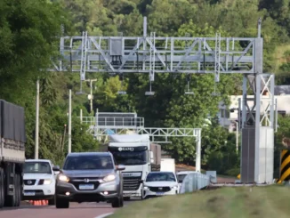 Rodovia com veículos em direção a um pórtico de pedágio eletrônico, com estrutura de cobrança Free Flow ao fundo, em cenário de tráfego no Brasil