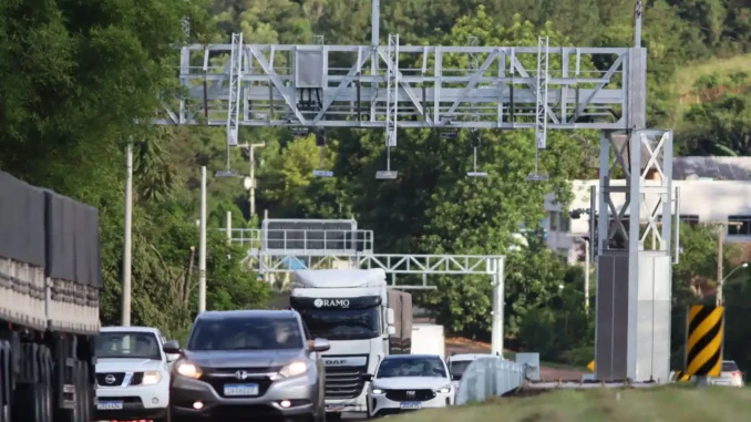 rodoia-veiculos-pedagio-eletronico-free-flow Rodovia com veículos em direção a um pórtico de pedágio eletrônico, com estrutura de cobrança Free Flow ao fundo, em cenário de tráfego no Brasil