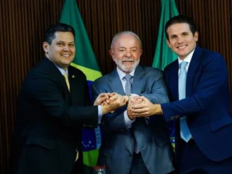 Lula cumprimenta lideranças do Congresso em cerimônia, com bandeiras ao fundo e os três homens de terno sorrindo durante o anúncio de união após a reeleição de Lula.
