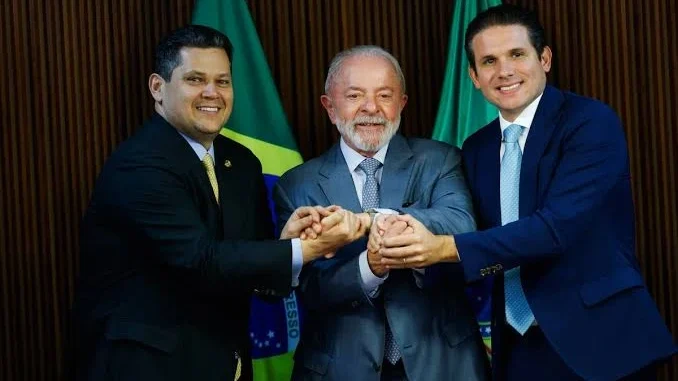 Lula cumprimenta lideranças do Congresso em cerimônia, com bandeiras ao fundo e os três homens de terno sorrindo durante o anúncio de união após a reeleição de Lula.